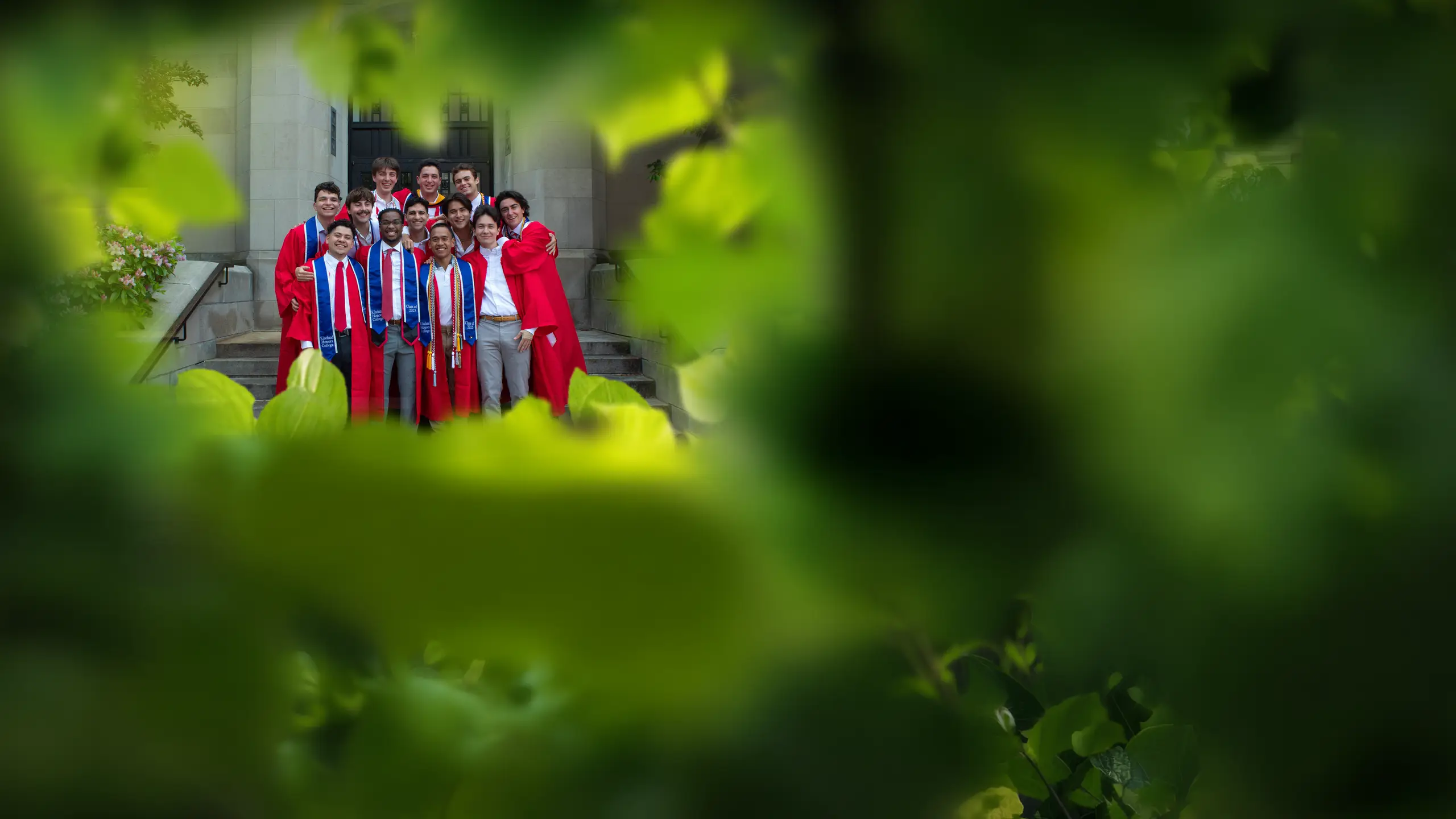 The group in graduation gowns on the steps, seen through the leaves